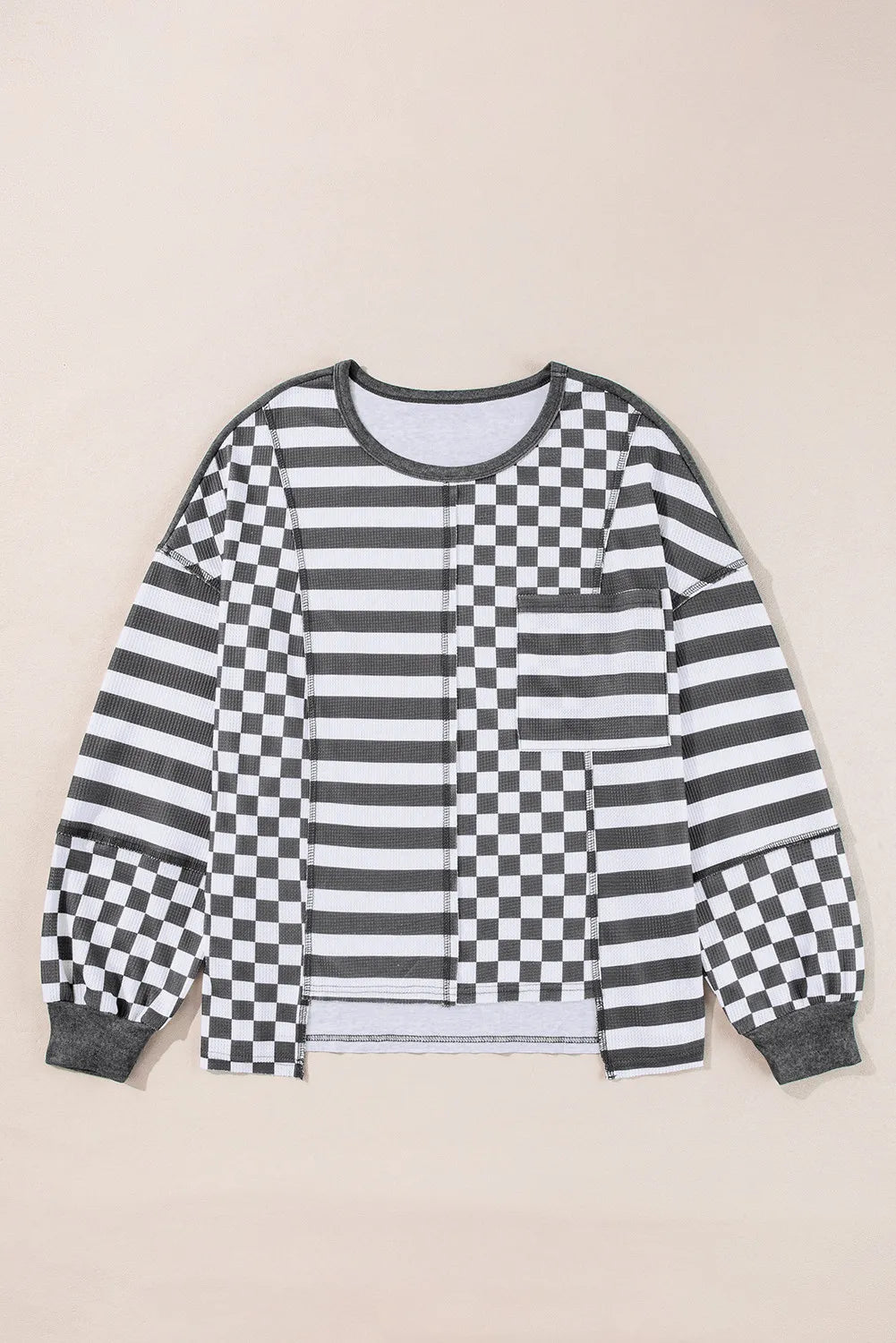 Asymmetrical knit top in black with patchwork stripes and checkerboard pattern.