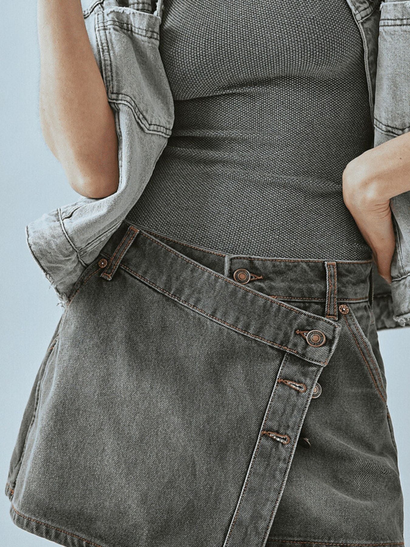 Gray denim skort with asymmetrical button-front detail and visible stitching.