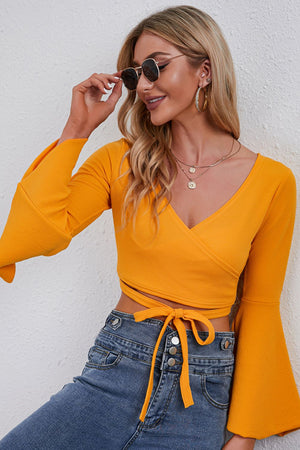 Wrap tie bell sleeve crop top in pumpkin orange with a V-neck and tie waist.