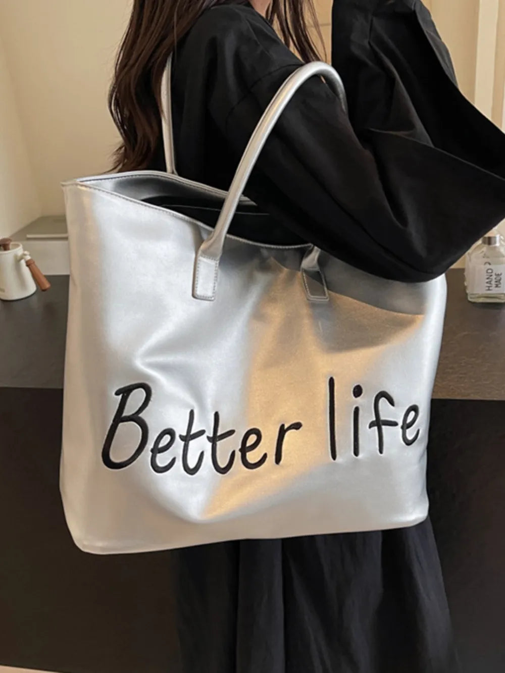 Silver metallic tote bag with "Better Life" graphic and dual straps.
