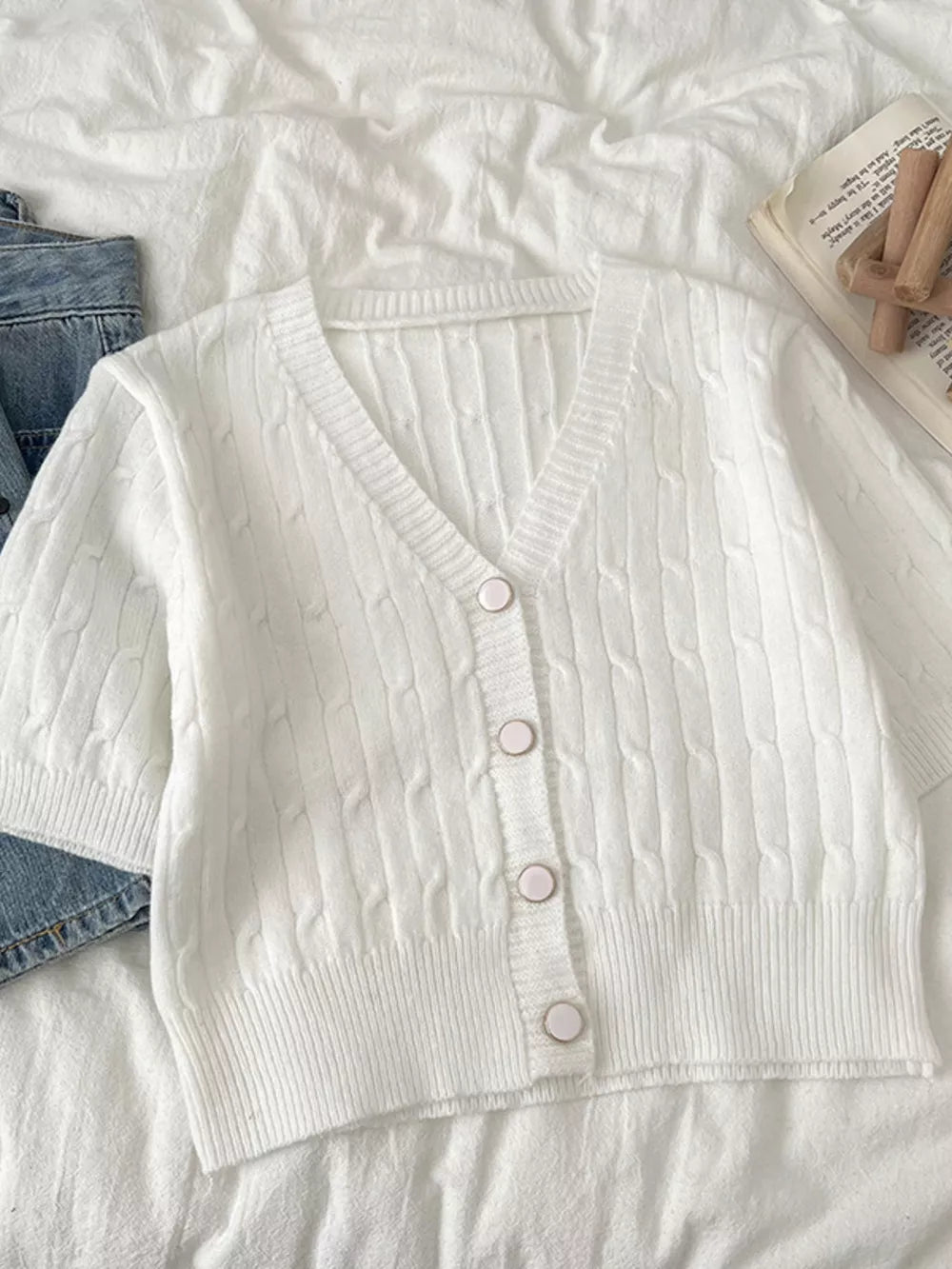 White cable-knit cropped cardigan with V-neck and button front.
