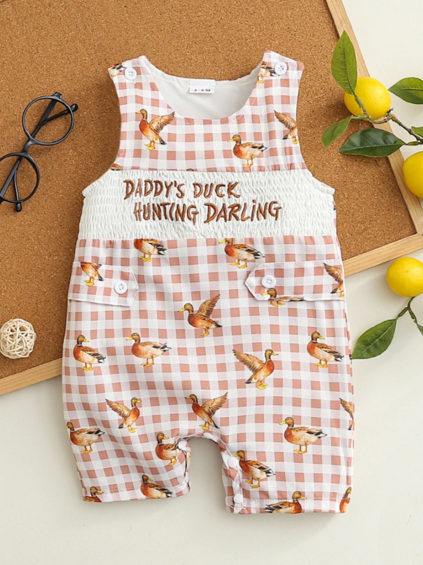 Baby one-piece with duck print on pink gingham, smocked waist, and button details.