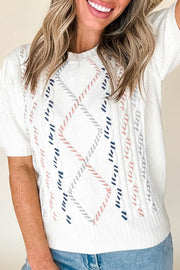 White cable knit sweater with puff sleeves and diamond pattern in pink, blue, and gray stitching.
