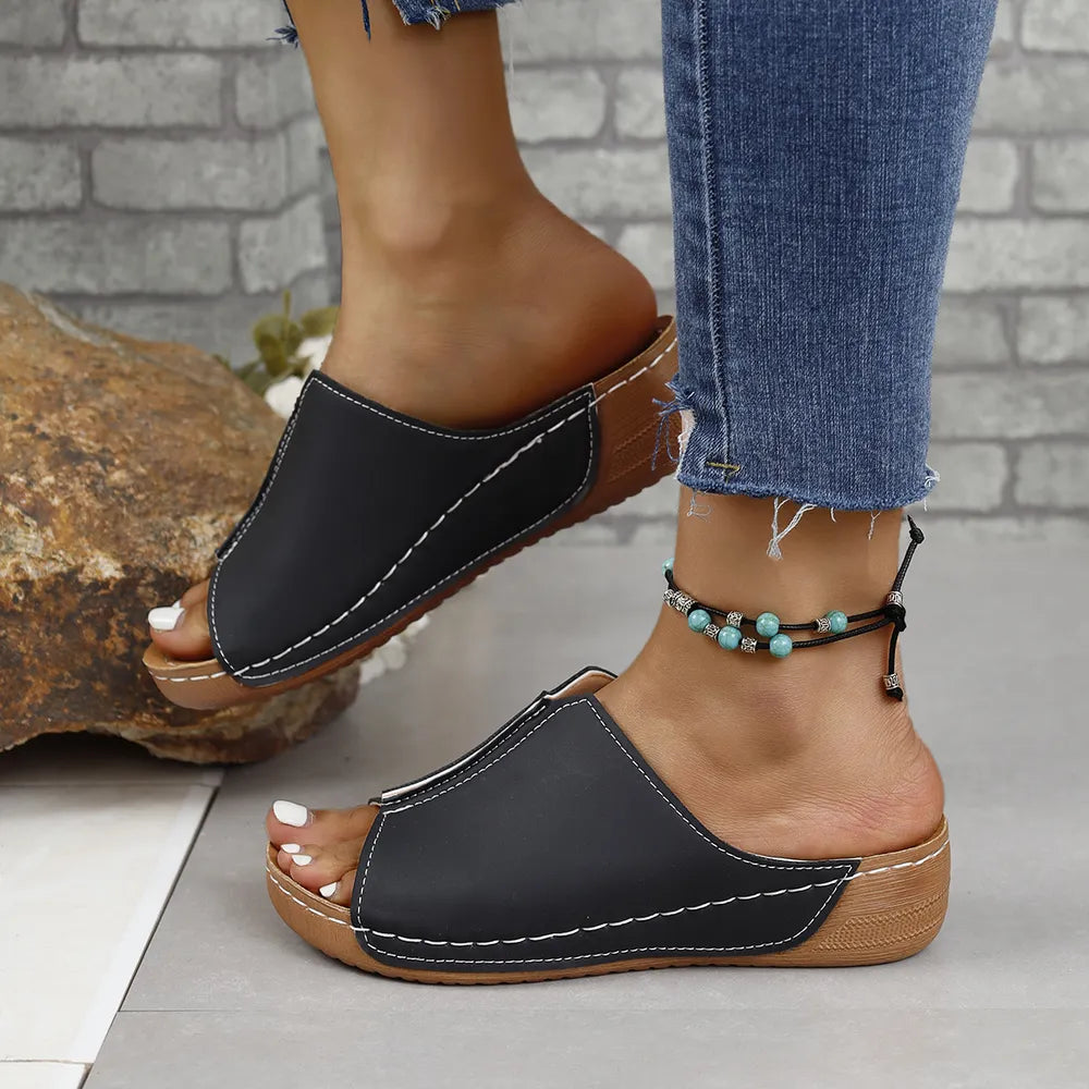 Black vegan leather asymmetrical slides with white stitching and peep toe.