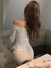 Off-shoulder white knit top with ruffled cuffs and shirred bodice.