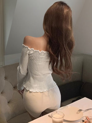 Off-shoulder white knit top with ruffled cuffs and shirred bodice.