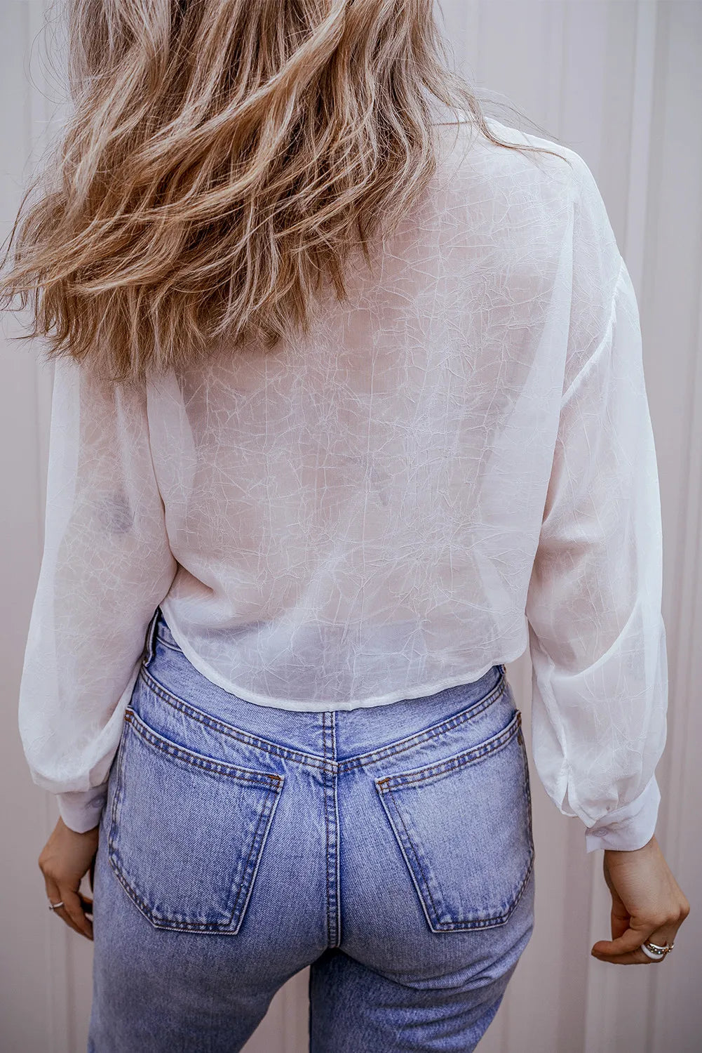 White sheer blouse with gathered sleeves and subtle textured pattern, styled with high-waisted jeans.