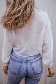 White sheer blouse with gathered sleeves and subtle textured pattern, styled with high-waisted jeans.