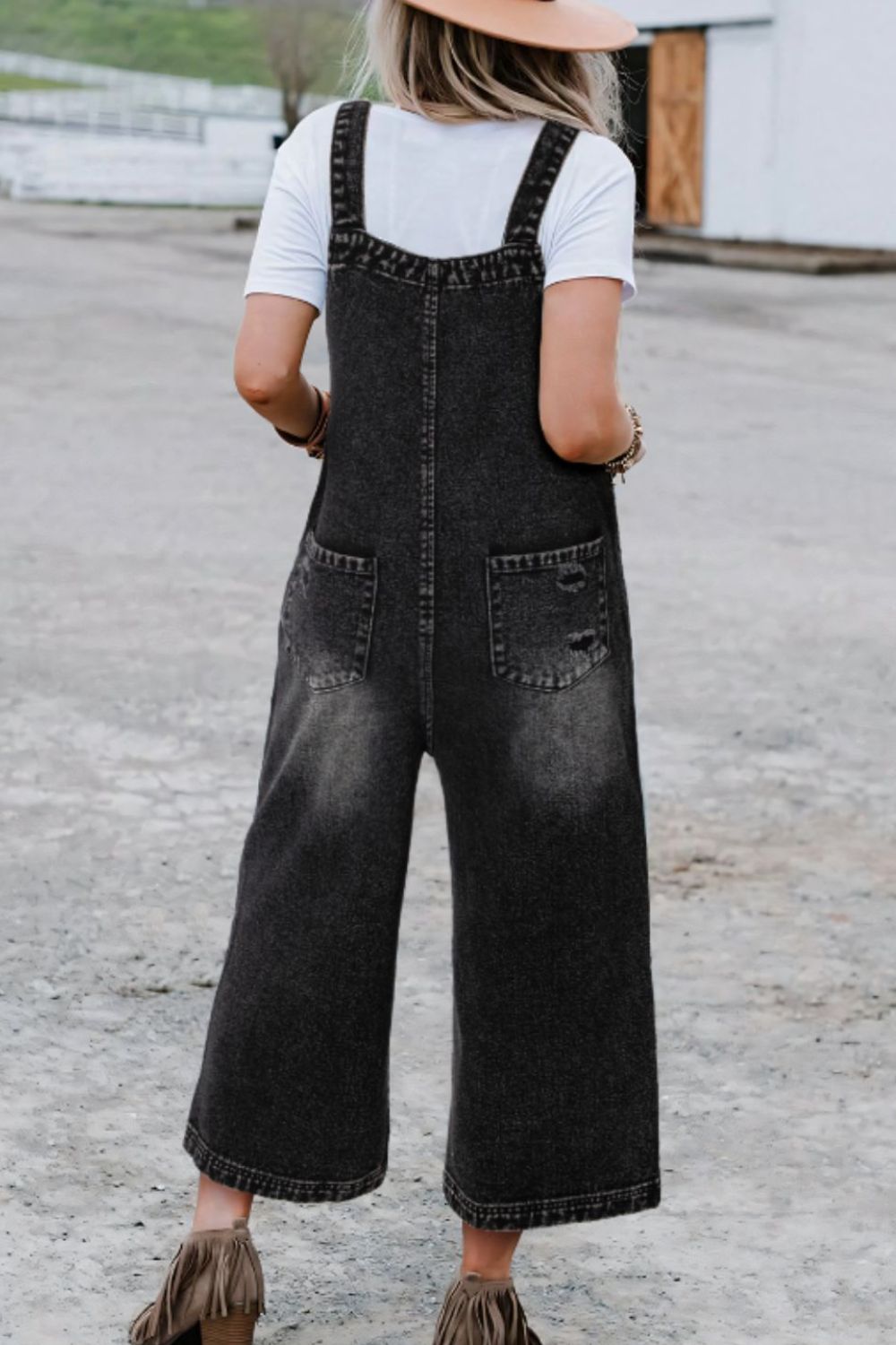 Black distressed denim culotte overalls with wide legs and back pockets.
