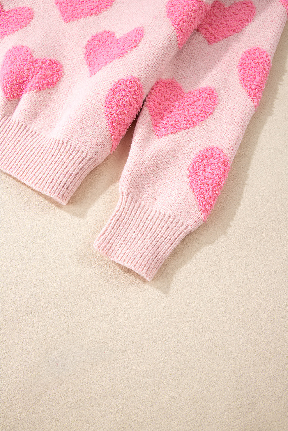 Blush pink knit sweater with textured heart motif and ribbed cuffs.