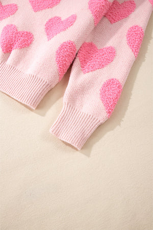 Blush pink knit sweater with textured heart motif and ribbed cuffs.