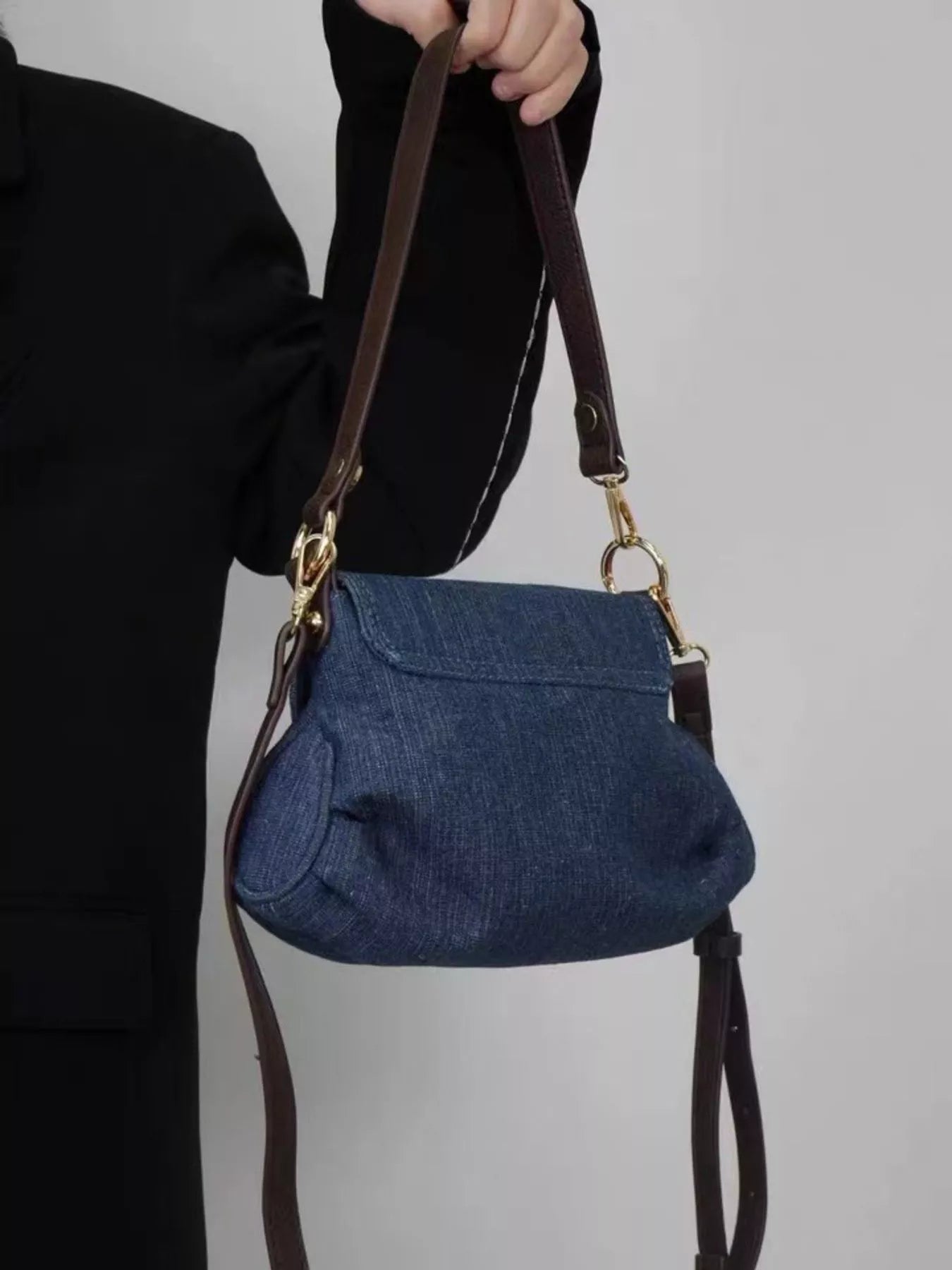 Mini denim shoulder bag with flap closure and brown leather straps.