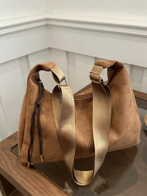 Brown suede crossbody bag with adjustable strap and drawstring detail.