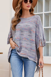 Multicolor knit poncho with fringe details and a boat neck, styled with jeans.
