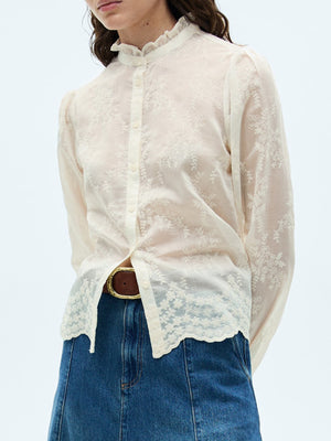 Sheer apricot blouse with floral embroidery, button front, and ruffled collar.
