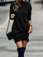 Black turtleneck mini dress with long sleeves and asymmetrical hem, styled with a quilted handbag.