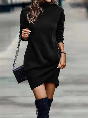 Black turtleneck mini dress with long sleeves and asymmetrical hem, styled with a quilted handbag.