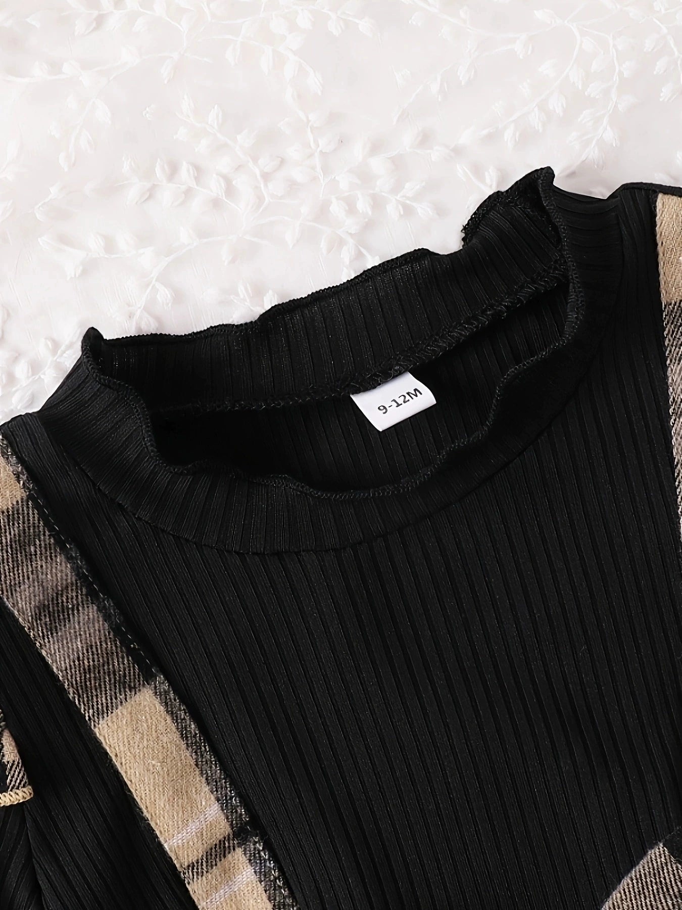 Black ribbed baby dress with ruffled neckline and plaid trim.