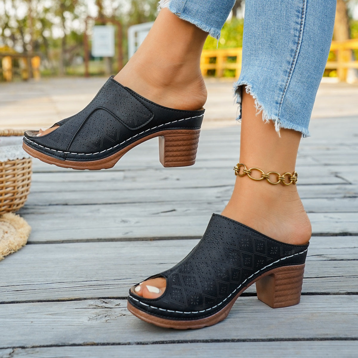Black peep-toe block heel mules with perforated detail and white stitching.