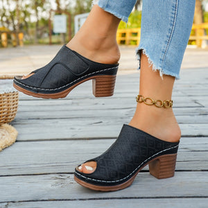 Black peep-toe block heel mules with perforated detail and white stitching.
