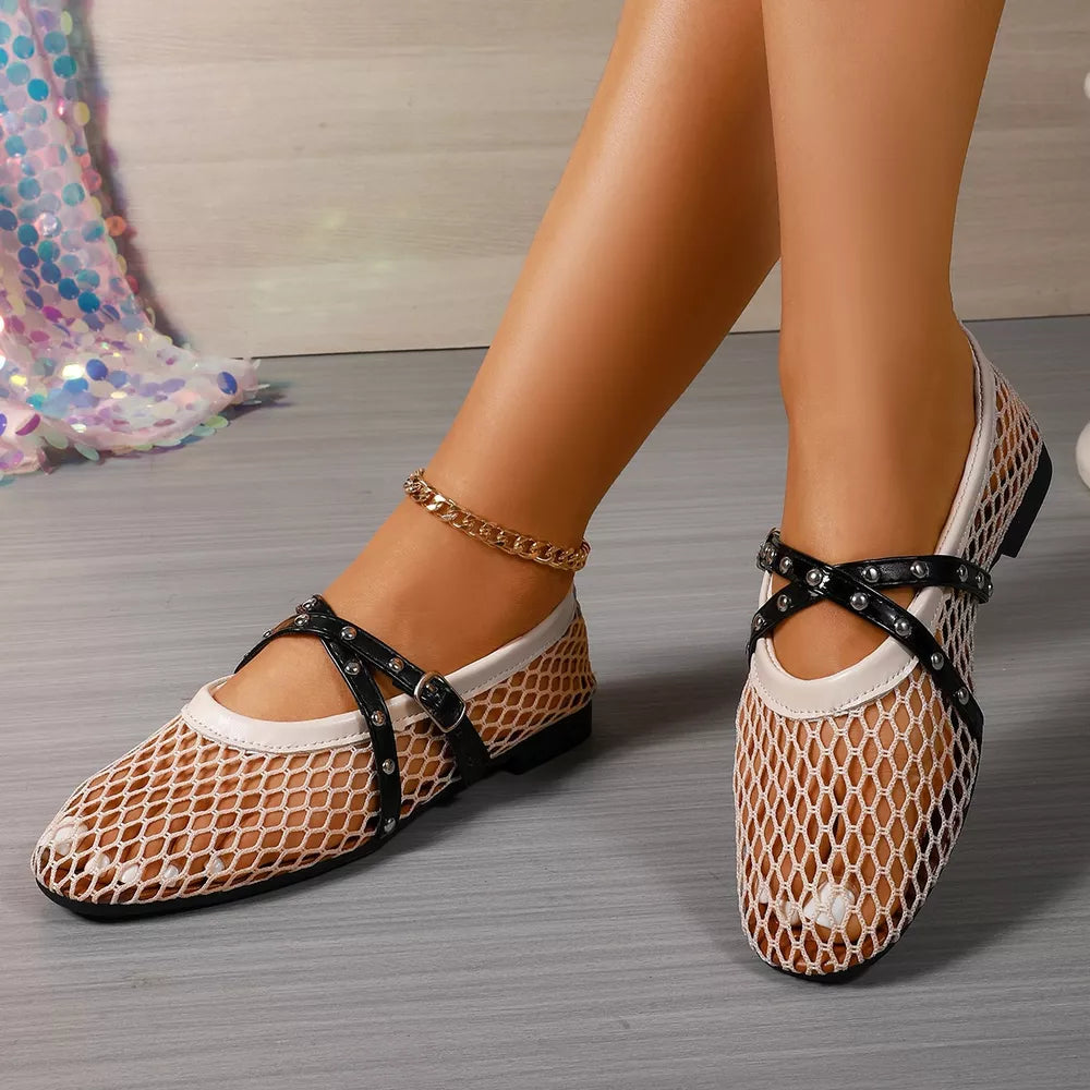Beige mesh slip-on flats with black studded crisscross straps and buckle detail.