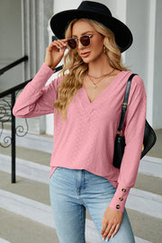 Blush pink diamond-textured V-neck blouse with button cuffs and long sleeves.
