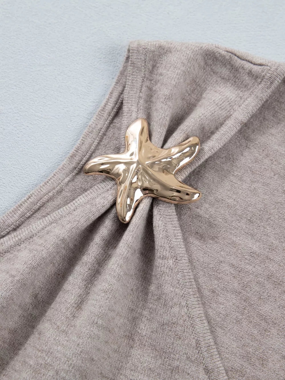 Grey V-neck knit vest with a gold starfish embellishment and draped detail.
