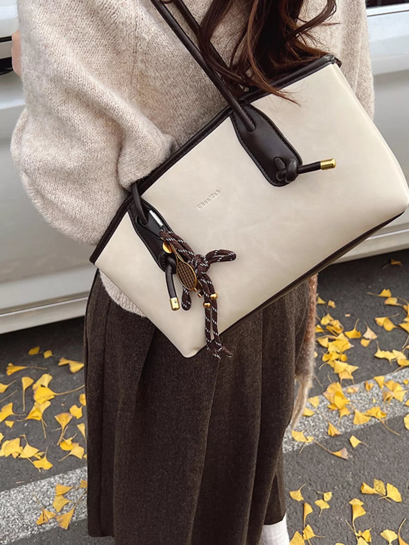 Beige leather shoulder bag with dark brown trim and a tennis racket charm.