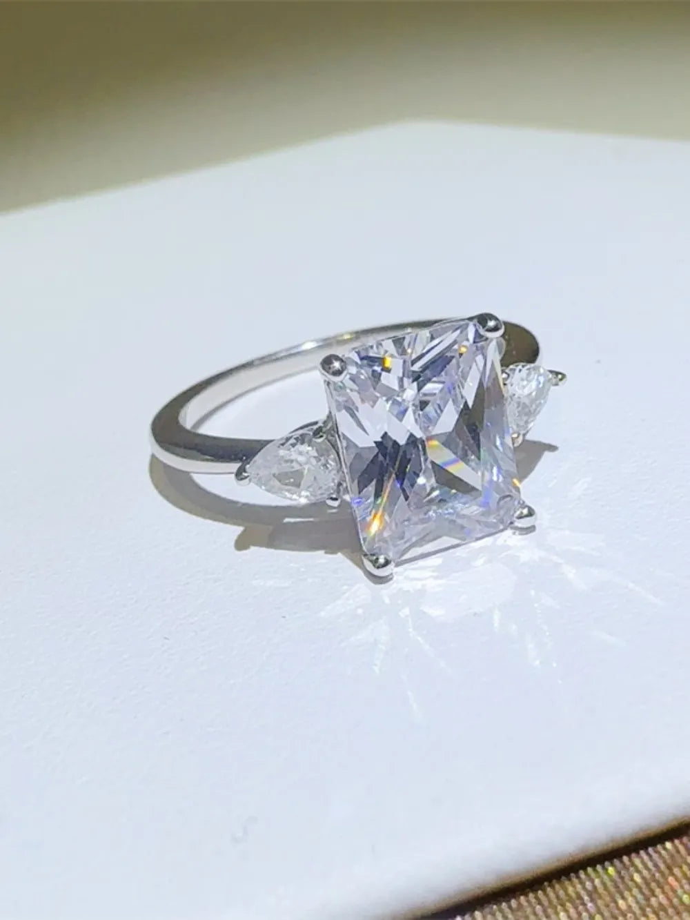 Silver ring with emerald cut center stone and pear accent stones.
