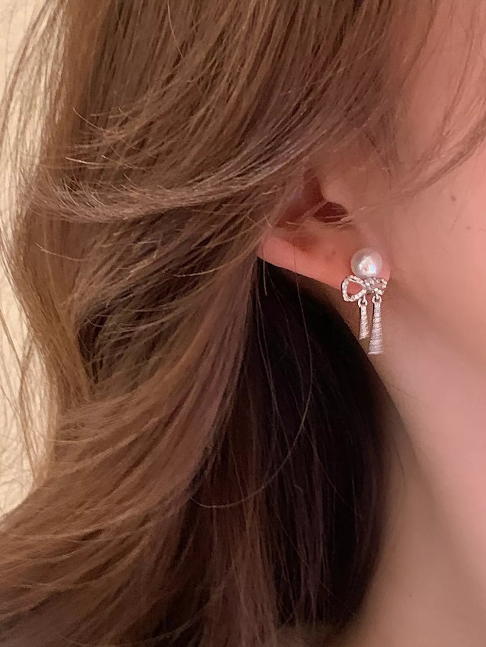 Luminous bowknot pearl drop earrings with silver accents and dangling charms.