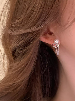 Luminous bowknot pearl drop earrings with silver accents and dangling charms.