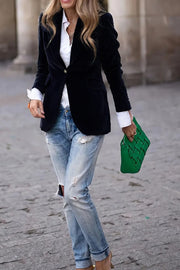 Black velvet blazer with gold button detail and notched lapels, worn open over a white shirt.