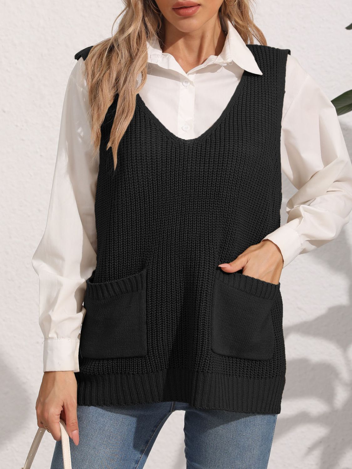 Black oversized knit vest with V-neck and patch pockets, styled over a white shirt.