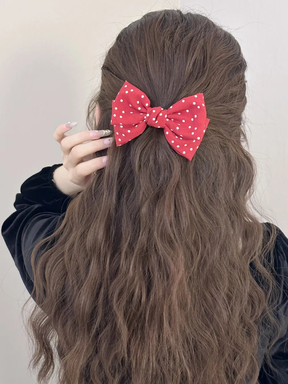 Deep red polka dot bow hair clip with white dots, styled in wavy brown hair.