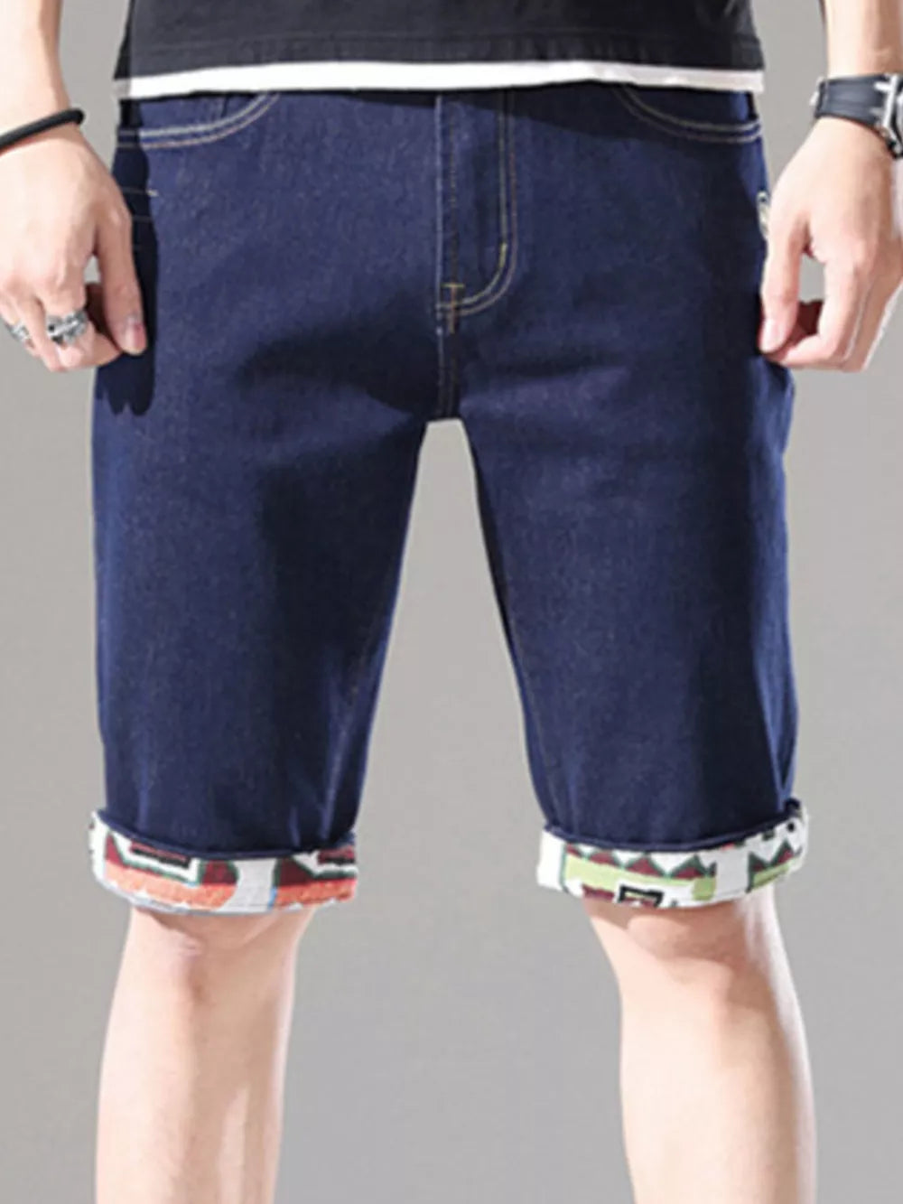 Men's dark blue denim shorts with rolled cuffs featuring a colorful geometric pattern.