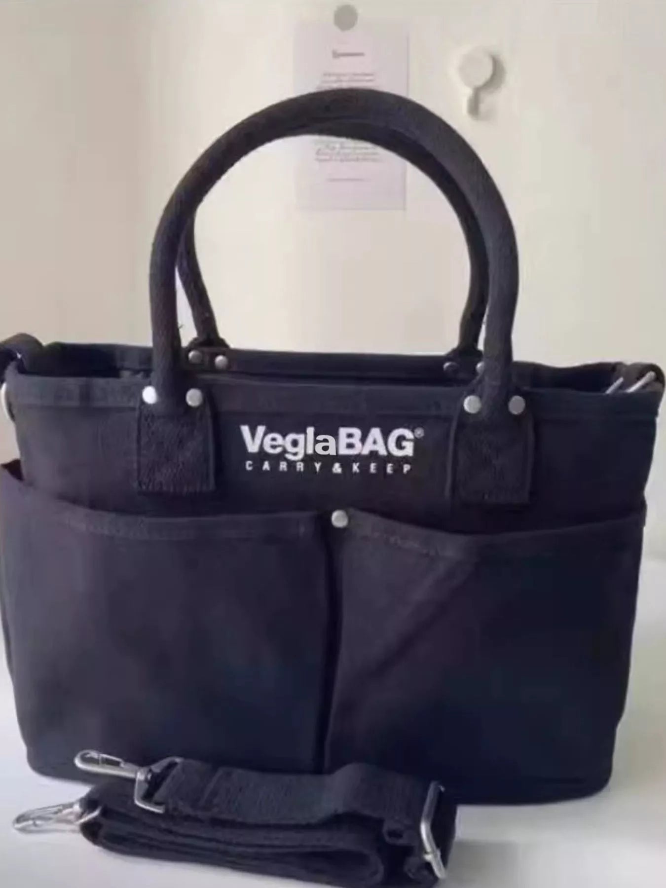 Black canvas shopper bag with multiple exterior pockets and top handles.