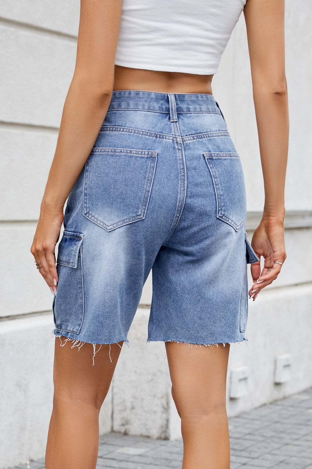 Medium wash denim bermuda shorts with raw hem and cargo pockets