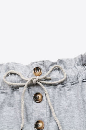 Light gray paperbag waist shorts with decorative buttons and drawstring detail.