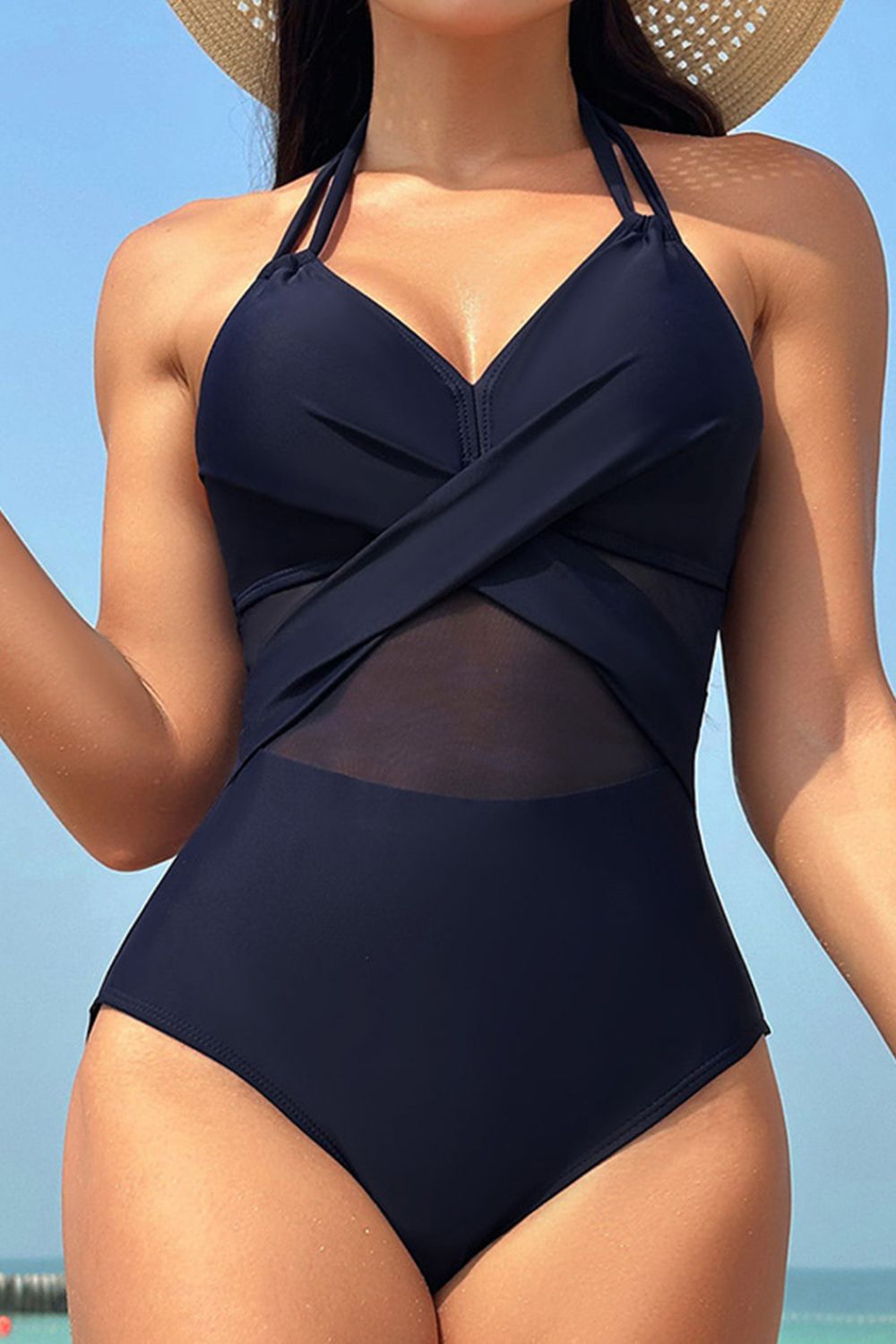 Dark blue one-piece swimsuit with crossover halter neckline and sheer mesh inset detail.