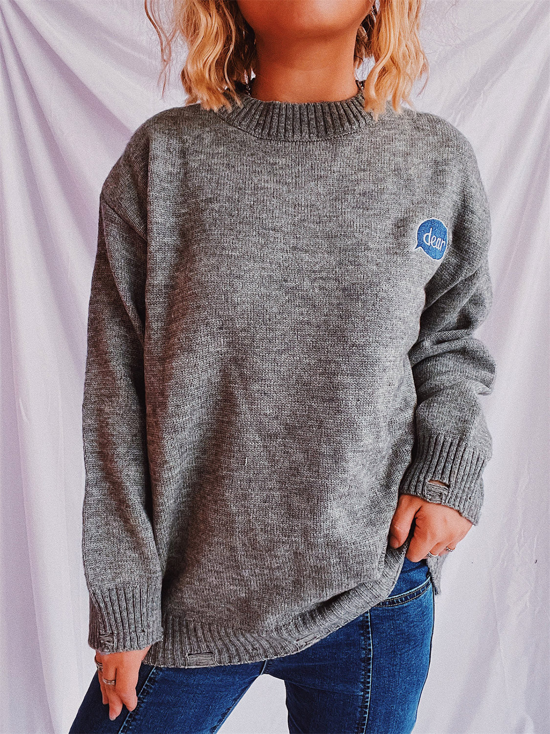 Dark gray relaxed knit sweater with embroidered blue speech bubble detail on chest.