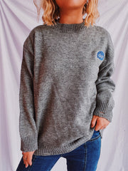 Dark gray relaxed knit sweater with embroidered blue speech bubble detail on chest.