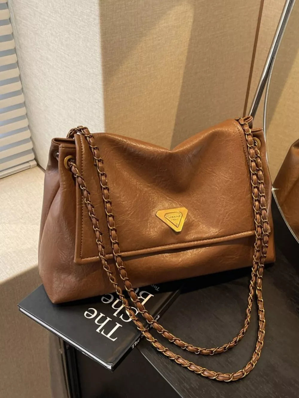 Brown leather shoulder bag with flap and chain detail.