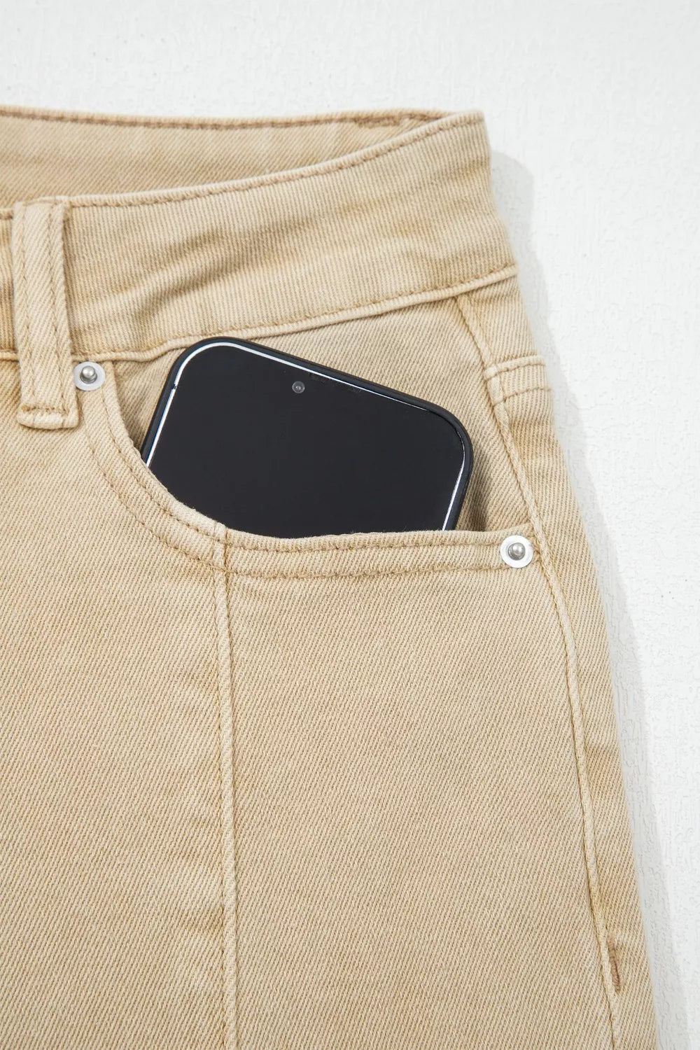 High-waisted cropped wide-leg jeans in tan denim with a phone in the pocket.