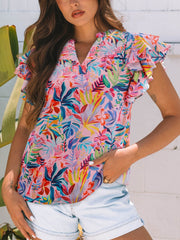 Pink cotton blouse with tropical floral print, V-neck, and ruffled short sleeves.