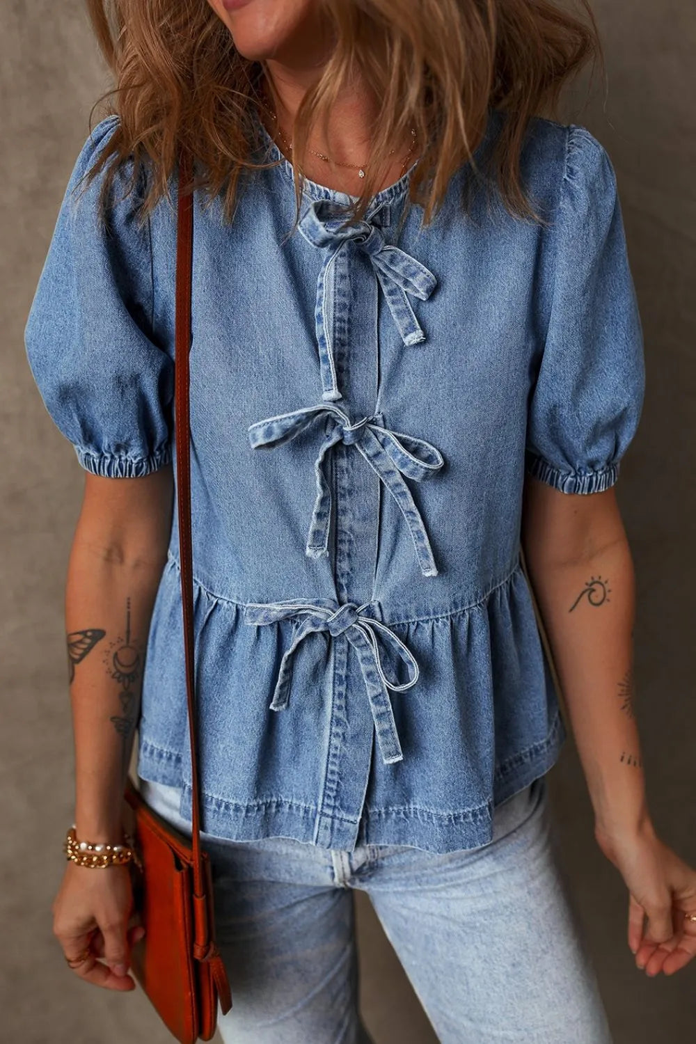 Denim peplum blouse in medium wash with puff sleeves and multiple bow tie details.