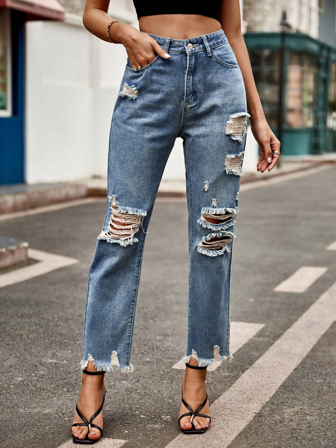 Medium wash denim jeans with ripped knees and raw hem straight leg cut.