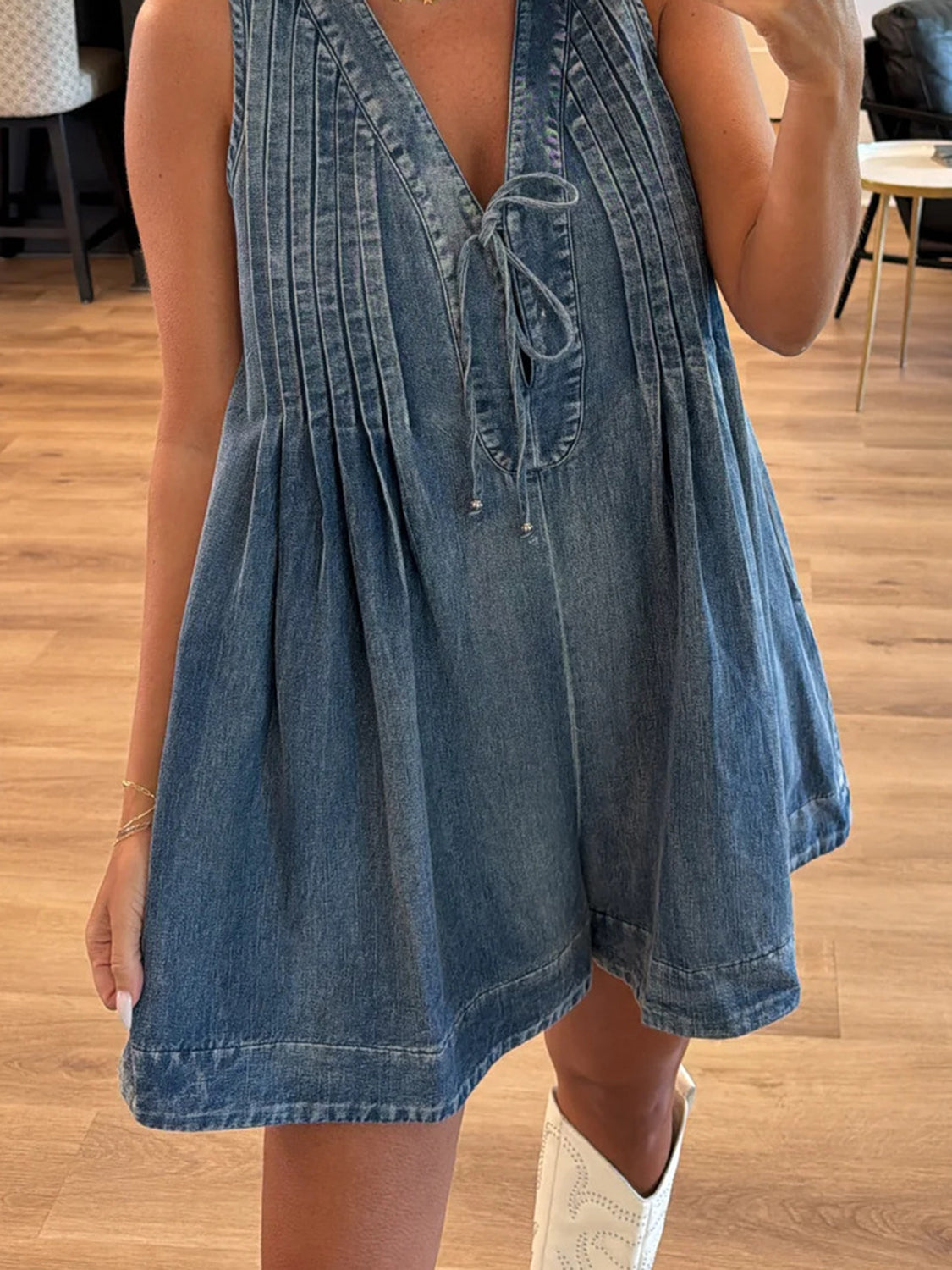 Light blue denim playsuit with V-neck, tie front, and pleated details.
