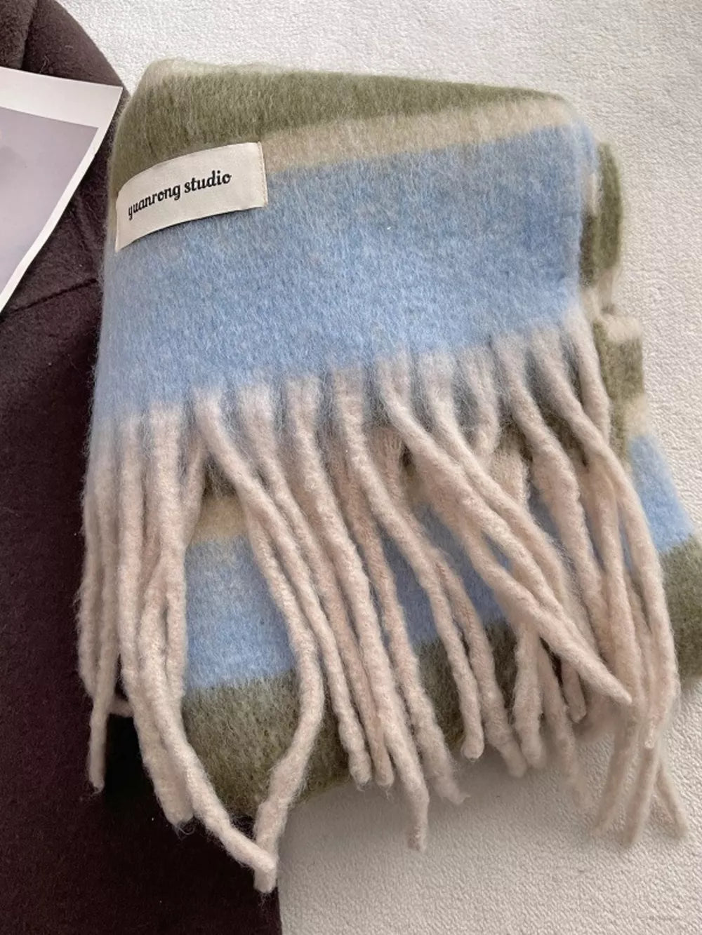 Plush striped scarf in green, blue, and tan with fringe detail.