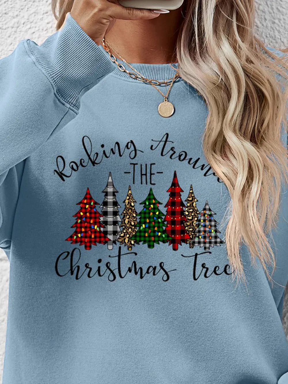 Misty Blue crewneck sweatshirt with a graphic of Christmas trees and text that reads Rocking Around the Christmas Tree.