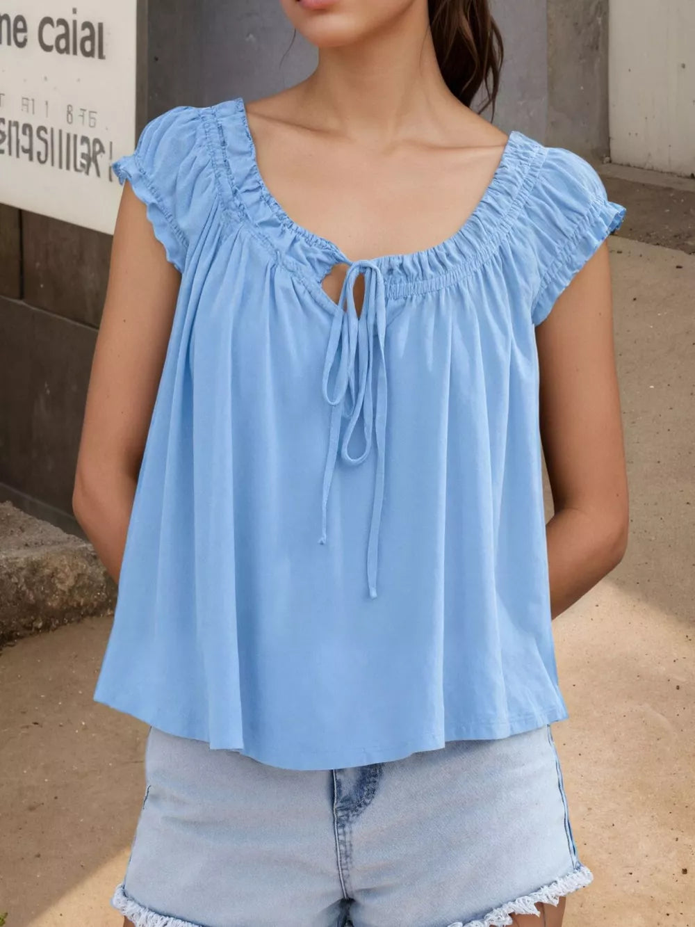 Blue gathered tie-front blouse with short sleeves and a scoop neckline.